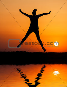 Silhouette woman jumping against orange sunset