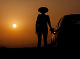 Silhouette woman with hat standing near car