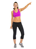 Full length portrait of smiling fitness young woman pointing on 