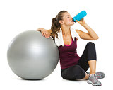 Fitness young woman with fitness ball drinking water