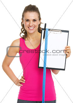 Happy fitness trainer showing blank clipboard with measure tape