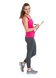 Full length portrait of smiling fitness trainer writing in clipb
