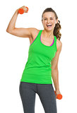 Happy fitness young woman with dumbbells showing biceps