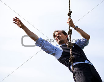 Determined businessman climbing a rope, reaching