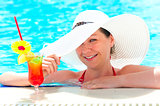 happy girl with a cocktail at the pool holding a hat hand