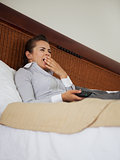 Yawing business woman laying on bed in hotel room and watching t
