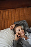 Business woman laying on bed in hotel room and talking cell phon