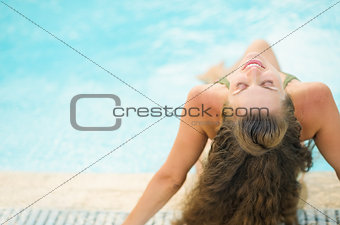 Happy young woman relaxing at poolside . rear view