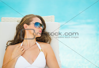 Young woman relaxing on chaise-longue at poolside