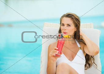 Young woman laying on chaise-longue and drinking cocktail