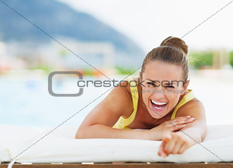 Smiling young woman laying on chaise-longue and pointing in came