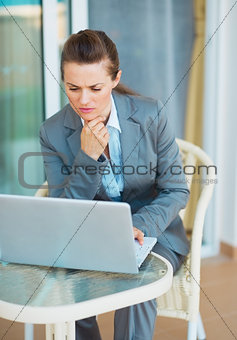 Thoughtful business woman looking on laptop on terrace