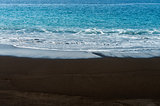 Black sand volcanic beach with white foam sea wave