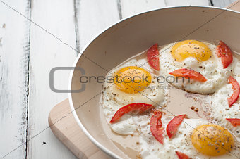 Hot pan with fried eggs and small pieces of tomato