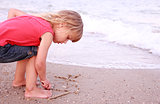 Little girl draws a sun in the sand on the beach