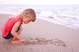 Little girl draws  in the sand on the beach