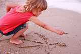 Little girl draws a sun in the sand on the beach