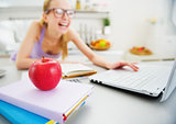 Closeup on apple and smiling young woman studying in kitchen in 