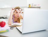 Surprised young woman looking in laptop while studying in kitche