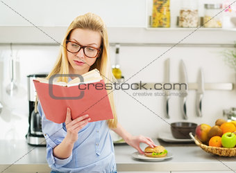 Teenager girl having sandwich in kitchen while studying