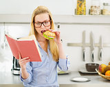 Teenager girl having burger in kitchen while studying