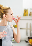 Young woman eating pill in kitchen