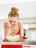 Laughing young woman eating popcorn and watching tv in kitchen