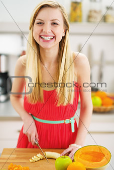 Smiling young woman cutting banana in kitchen