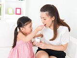Beautiful child feeding mother yogurt