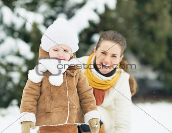 Happy mother and baby playing in winter outdoors