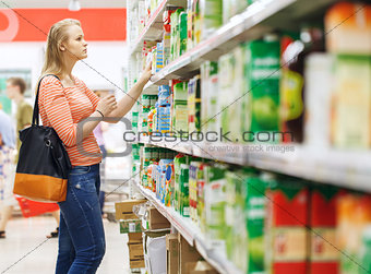 Young woman shopping for juice in supermarket