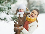 Happy mother and baby playing with snow on branch