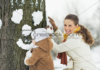 Happy mother and baby making face for tree using snow