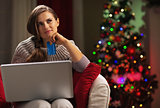 Thoughtful young woman with laptop and credit card near christma
