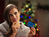 Portrait of thoughtful young woman with credit card near christm