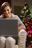 Smiling young woman near christmas tree using laptop