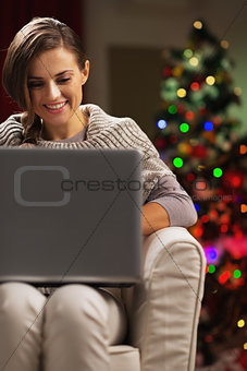 Smiling young woman near christmas tree using laptop