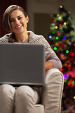 Happy young woman near christmas tree with laptop
