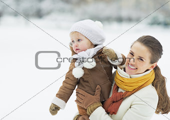 Happy mother holding baby looking on copy space in winter park