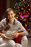 Happy young woman reading book near christmas tree
