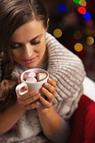 Young woman with cup of hot chocolate with marshmallow in front 