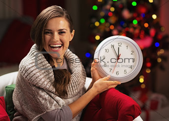 Smiling young woman near christmas tree showing clock