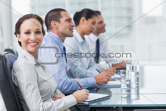 Businesswoman smiling at camera while her colleagues listening to presentation