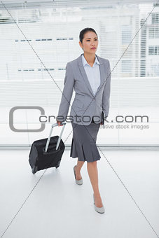 Serious businesswoman carrying her suitcase