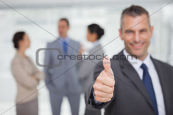 Smiling manager showing thumb up with employees in background