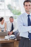 Cheerful businessman standing while his colleagues are working