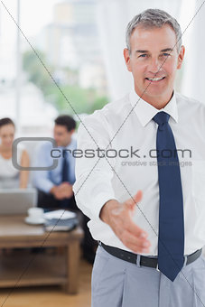 Executive standing on foreground holding out his hand