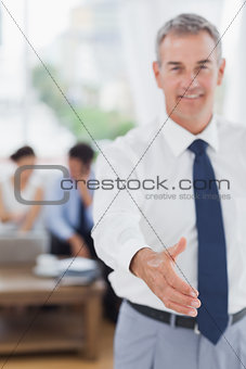 Executive standing on foreground holding out his hand to camera