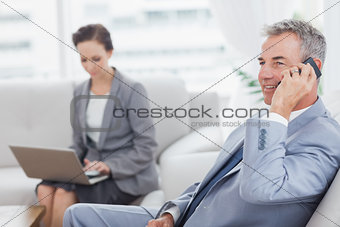 Businessman on the phone while his colleague working on her laptop