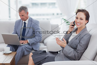 Businesswoman calling while her colleague working on his laptop